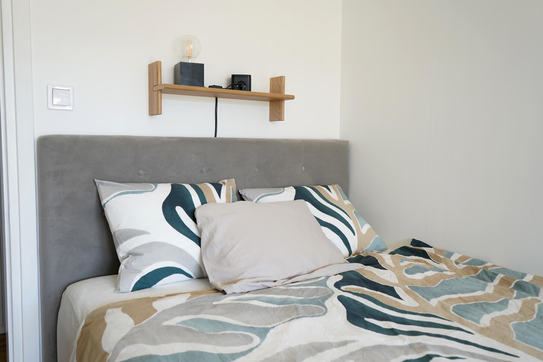 Close up of double bed with fresh linnen and a small shelf on the wall